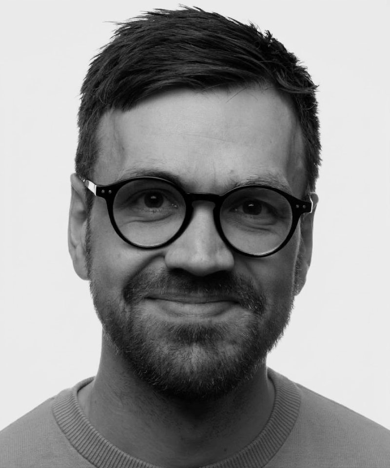 Henrik Hauge Hove, black-and-white portrait: short dark hair, round black glasses, a beard and a small smile.